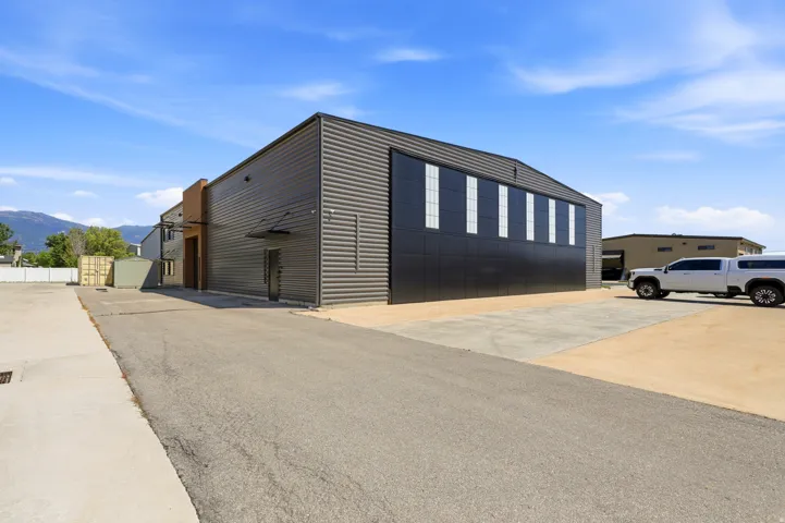 Industrial building featuring a corrugated metal exterior, multiple large windows, and an expansive paved lot