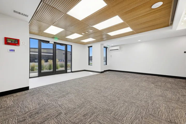 Spacious interior featuring a wood-slat ceiling with integrated rectangular lighting, full-light entry doors, large windows, and patterned carpet flooring