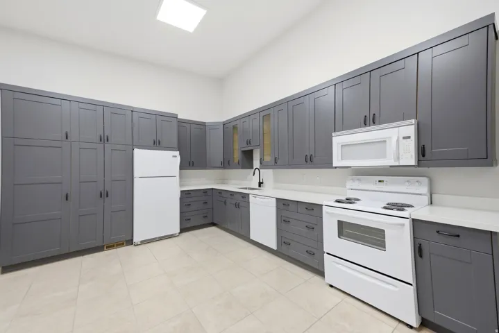 Open-concept kitchen featuring extensive gray shaker cabinetry, white countertops, and light-toned tile flooring
