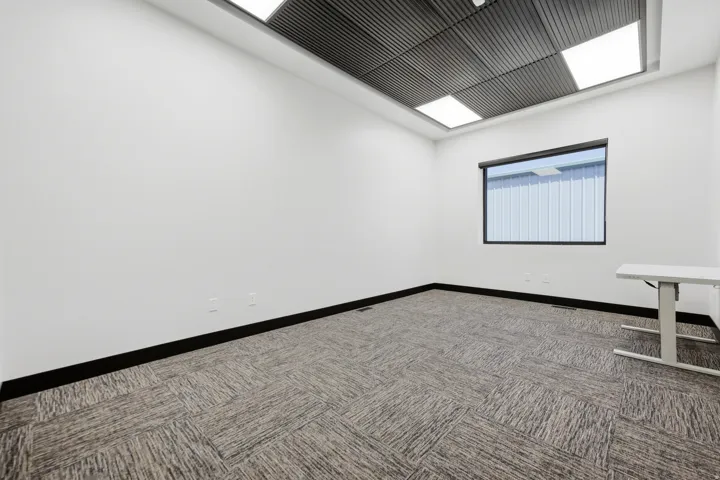 Room featuring modular carpet flooring, a black-framed window, and a suspended grid ceiling with integrated lighting