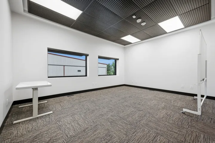 Spacious room featuring a textured acoustic ceiling, recessed lighting, two windows, neutral carpet flooring, and white walls