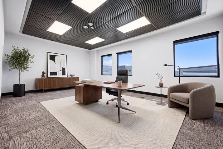 Office space featuring a suspended ceiling with recessed lighting, large windows with roller shades, and patterned carpet flooring
