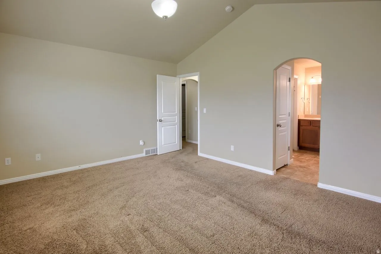 Unfurnished bedroom with arched walkways, lofted ceiling, light carpet, and ensuite bathroom