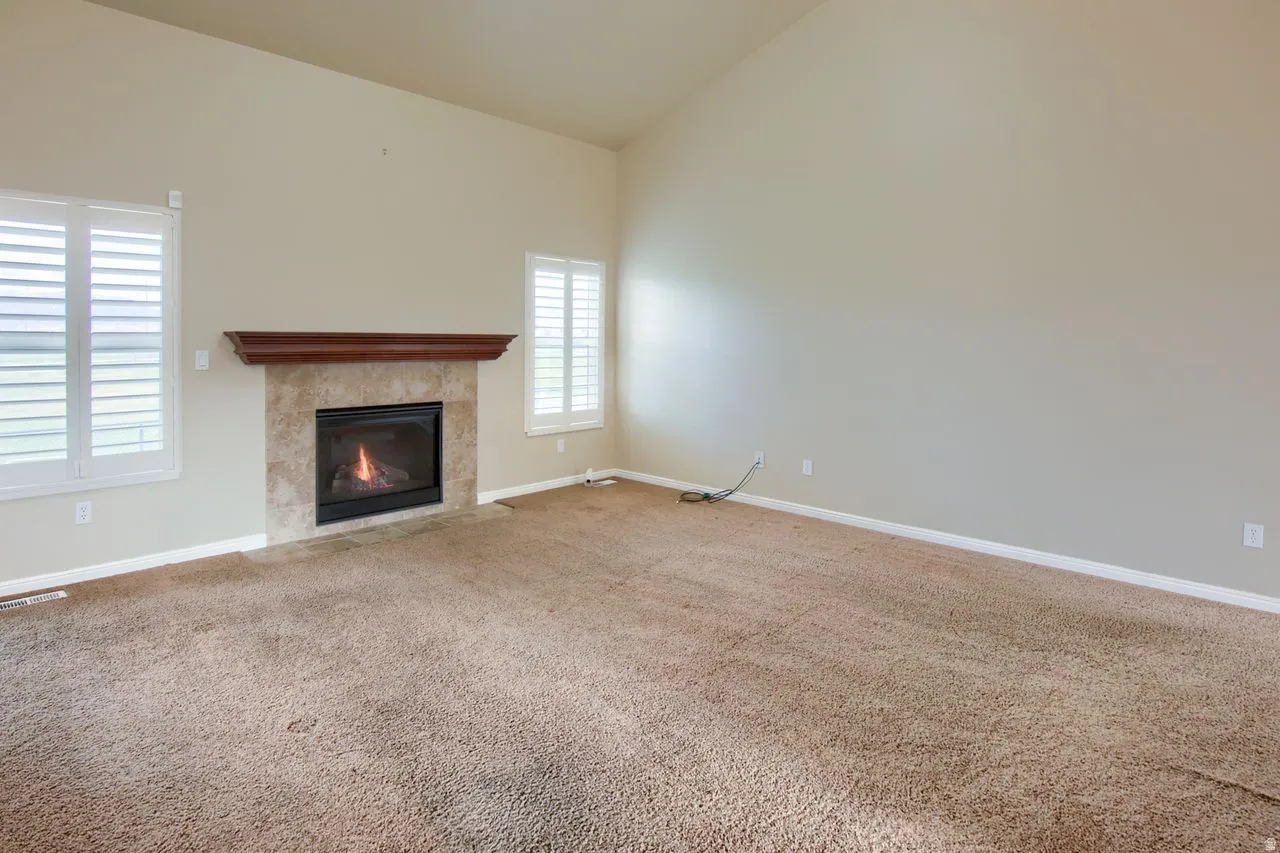 Unfurnished living room with lofted ceiling, a fireplace, and carpet