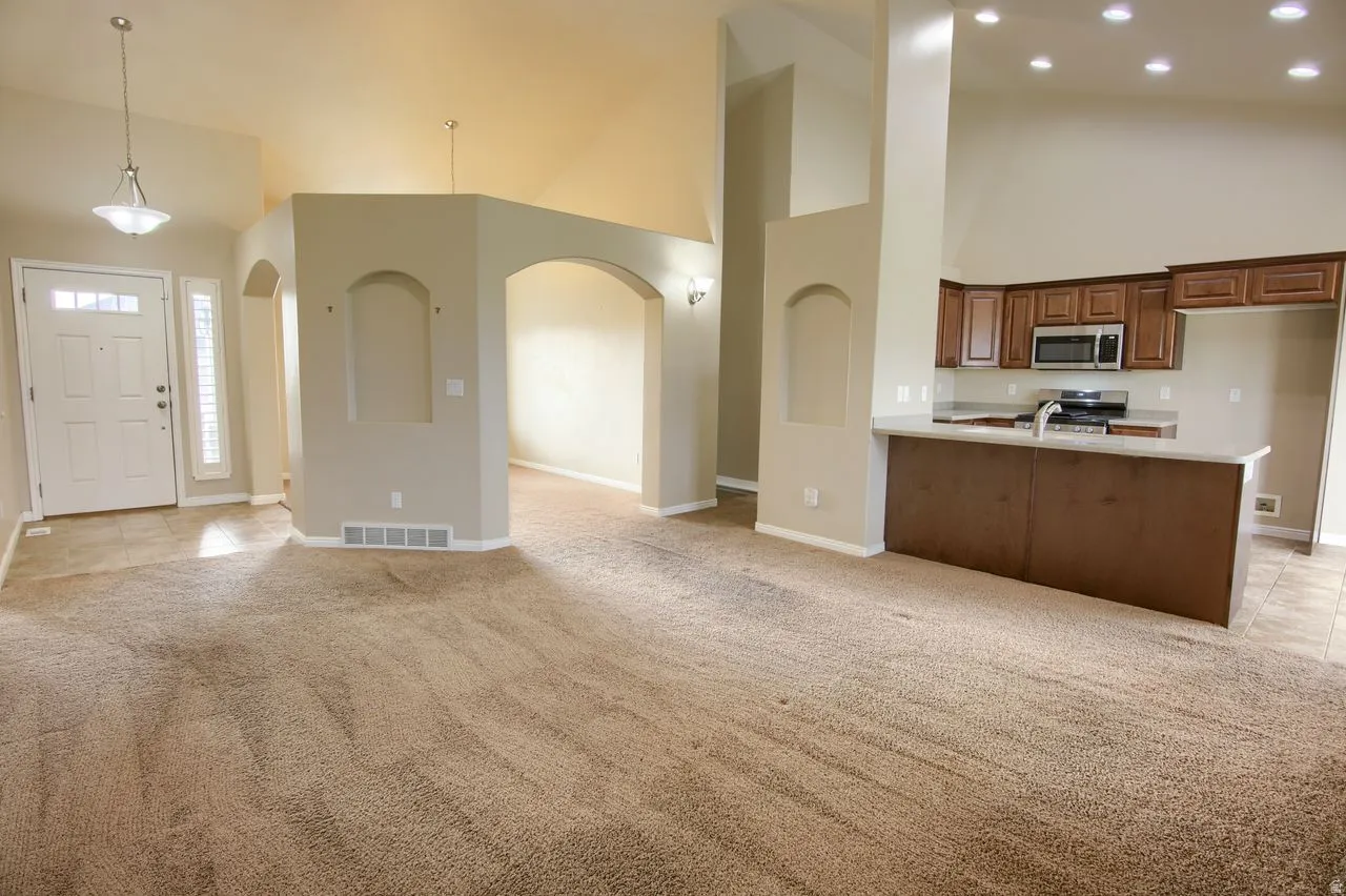 Kitchen with high vaulted ceiling, open floor plan, light carpet, a peninsula, and recessed lighting