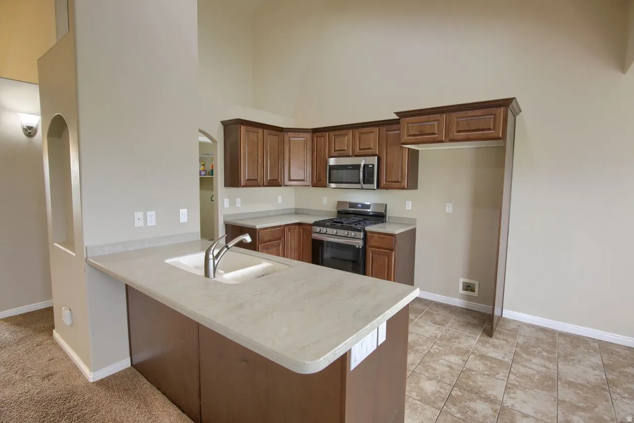 Kitchen with a peninsula, appliances with stainless steel finishes, light countertops, a high ceiling, and brown cabinets