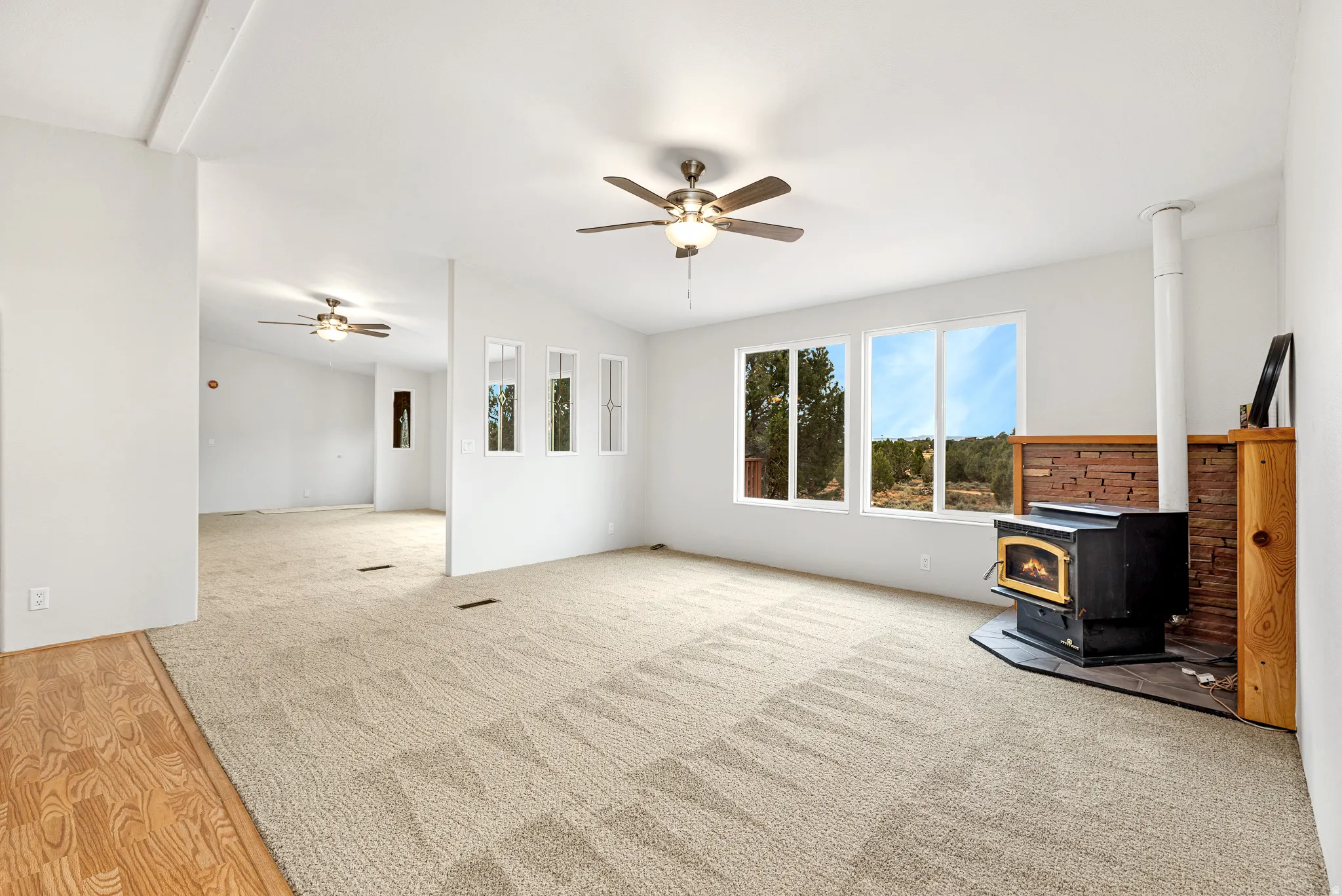 Unfurnished living room featuring a wood stove, carpet floors, and ceiling fan