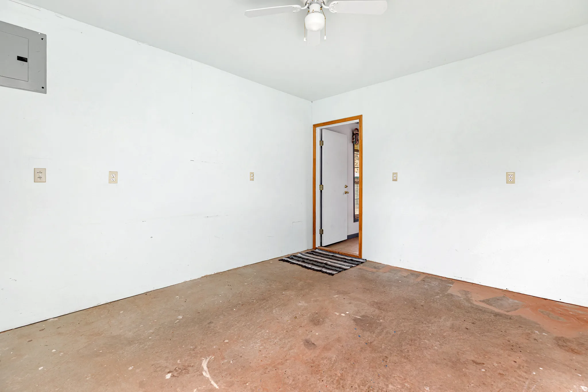 Spare room with electric panel, unfinished concrete flooring, and ceiling fan
