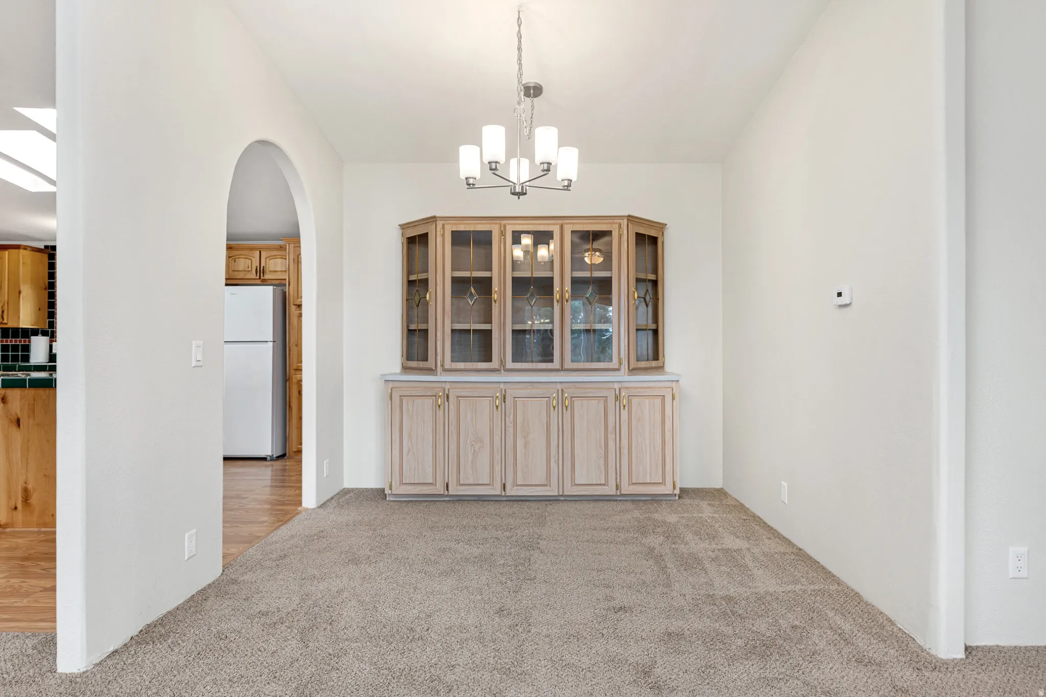 Unfurnished dining area featuring arched walkways, light colored carpet, and a chandelier