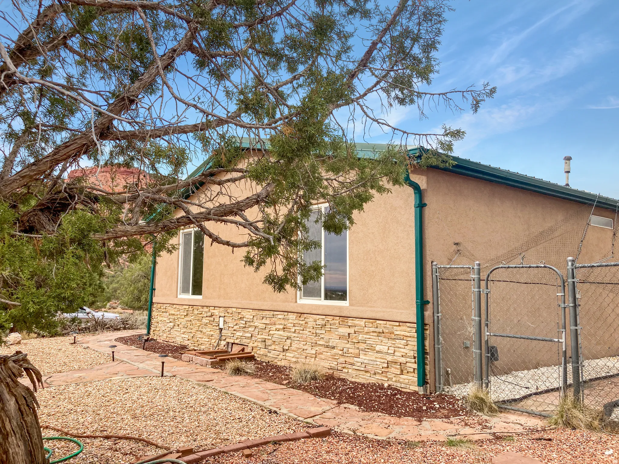 View of side of home featuring stone siding, a gate, and stucco siding