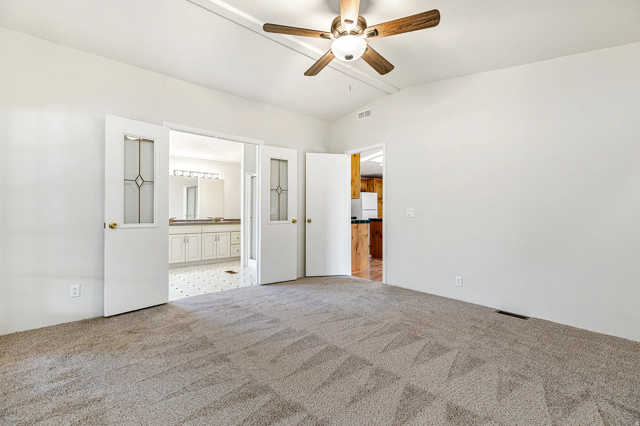 Unfurnished bedroom featuring light carpet, connected bathroom, a ceiling fan, and freestanding refrigerator