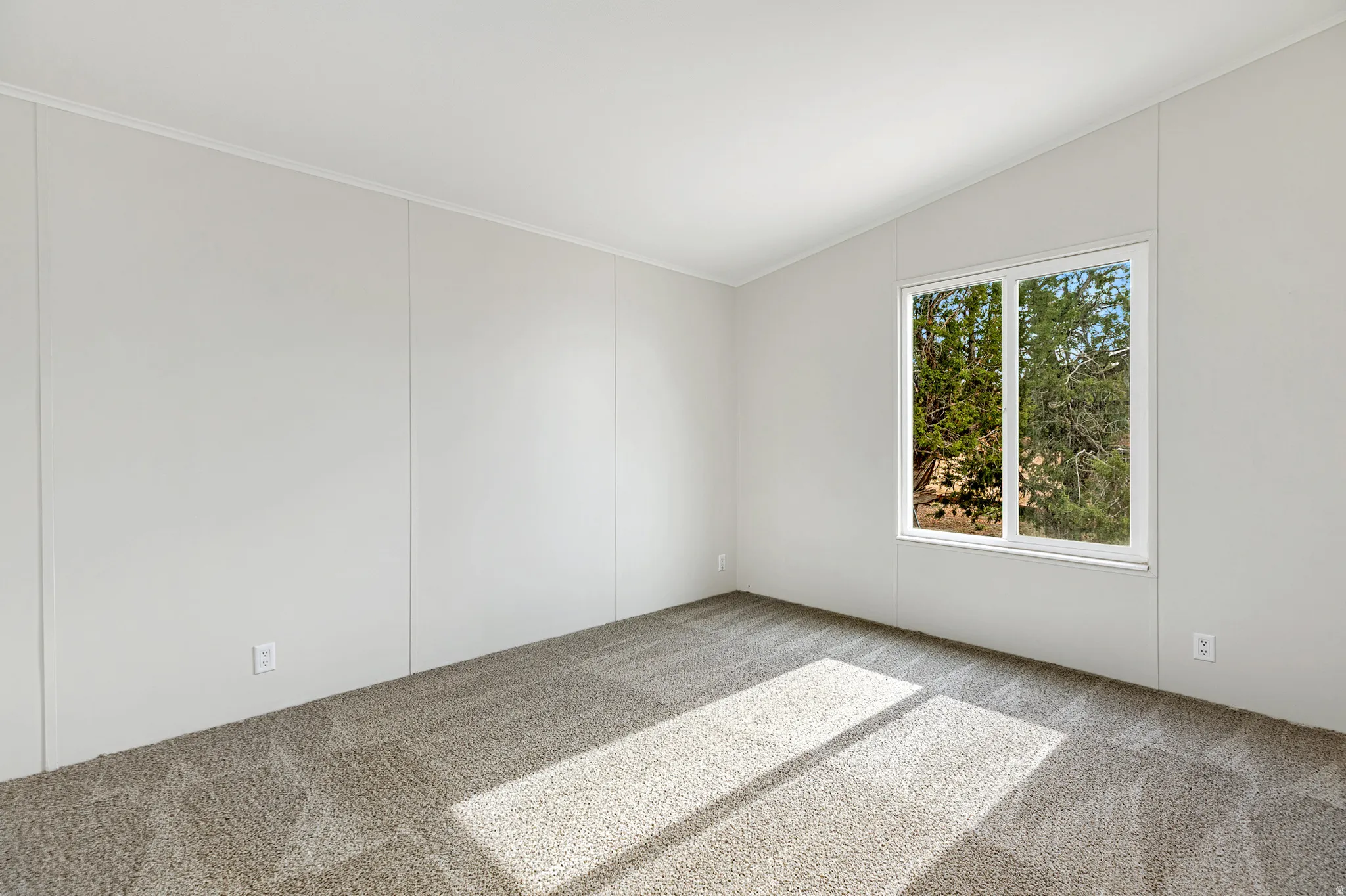 Empty room with vaulted ceiling and light colored carpet