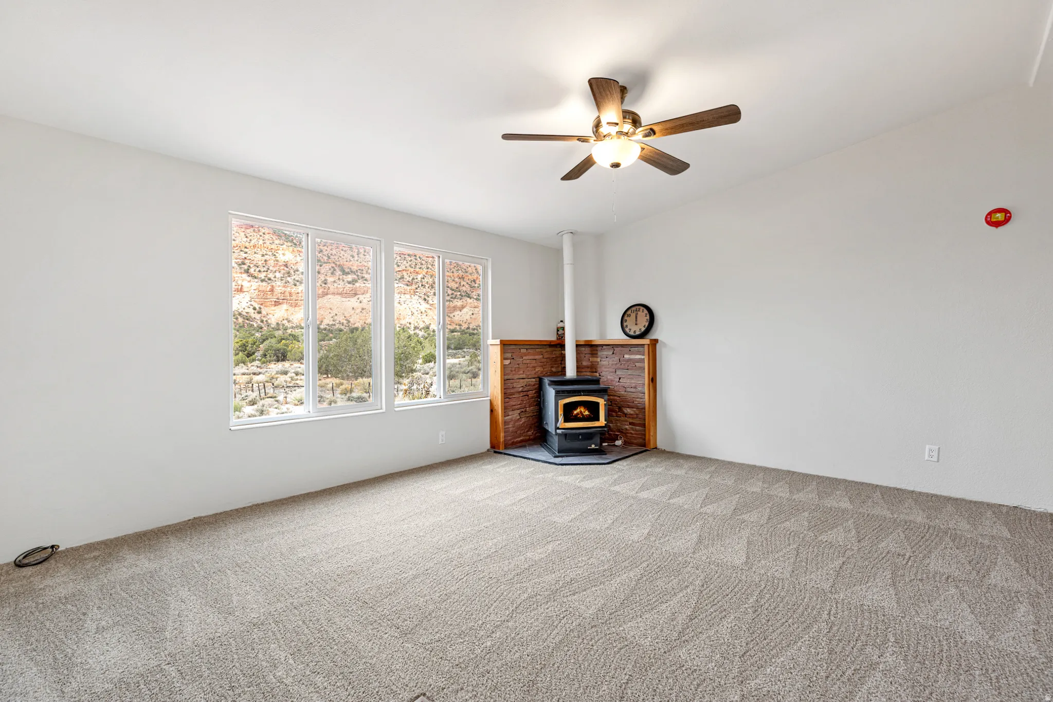 Unfurnished living room featuring a wood stove, carpet flooring, and ceiling fan