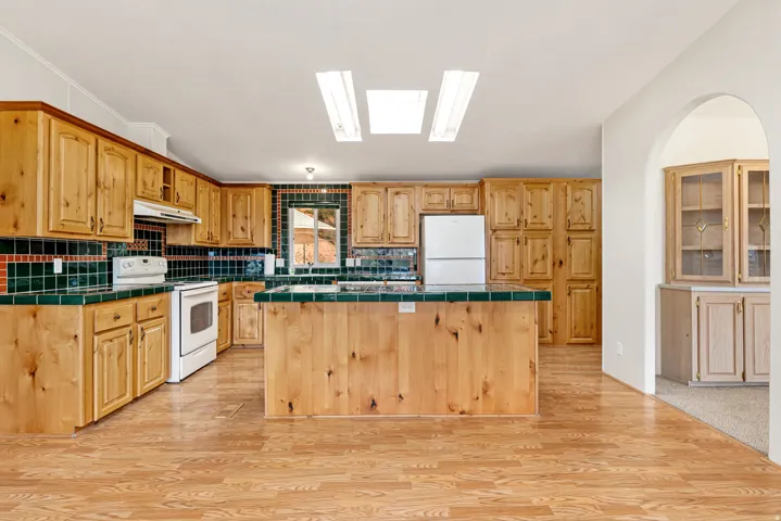 Kitchen with tile counters, white appliances, backsplash, a skylight, and lofted ceiling