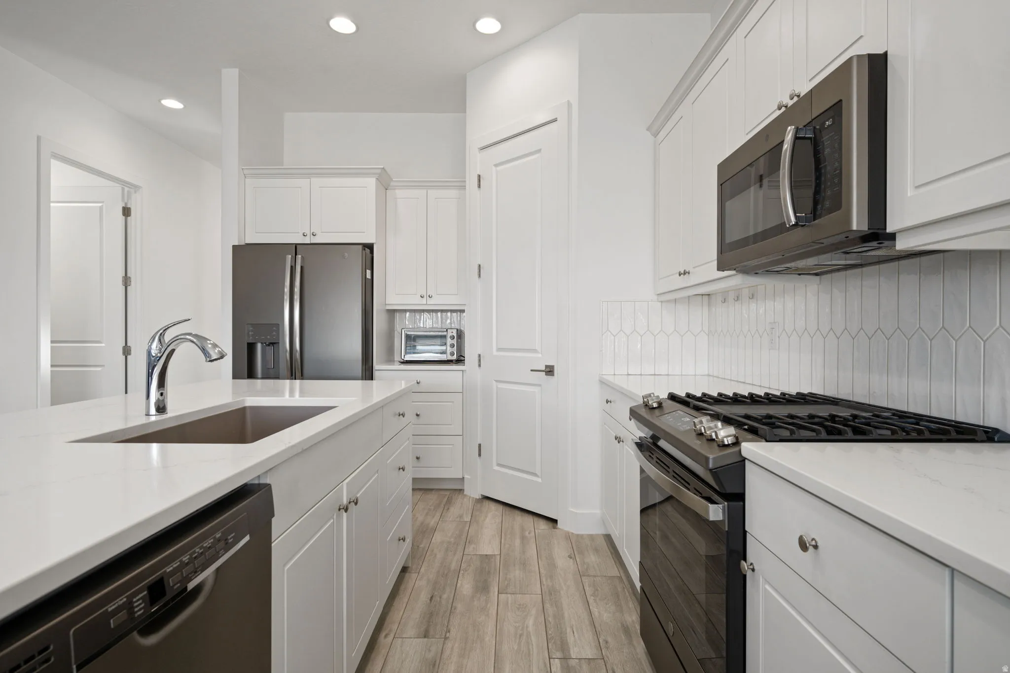 Kitchen featuring stainless steel appliances, recessed lighting, white cabinetry, light stone countertops, and light wood finished floors