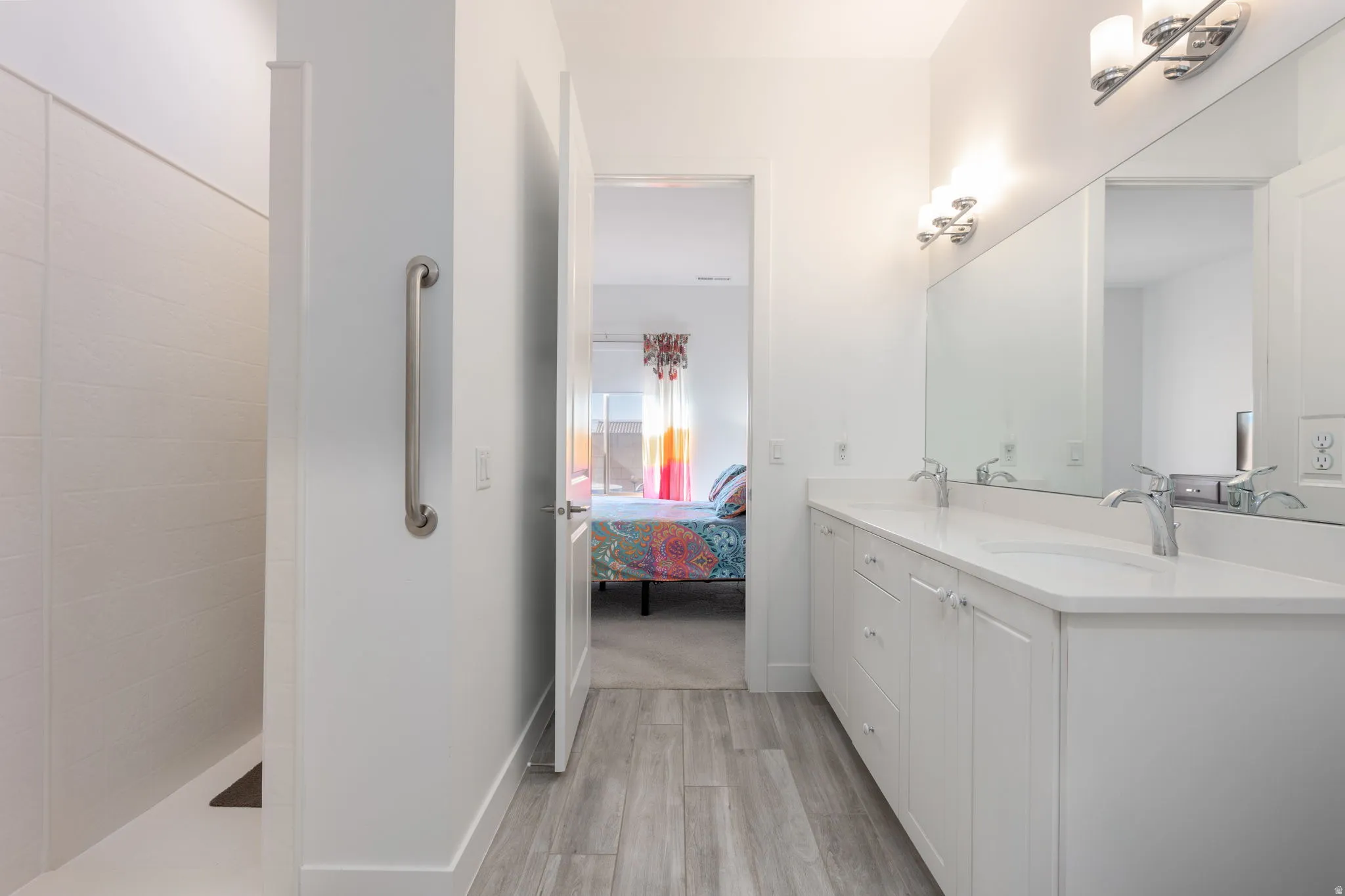 Bathroom with connected bathroom, light wood-style floors, double vanity, and walk in shower