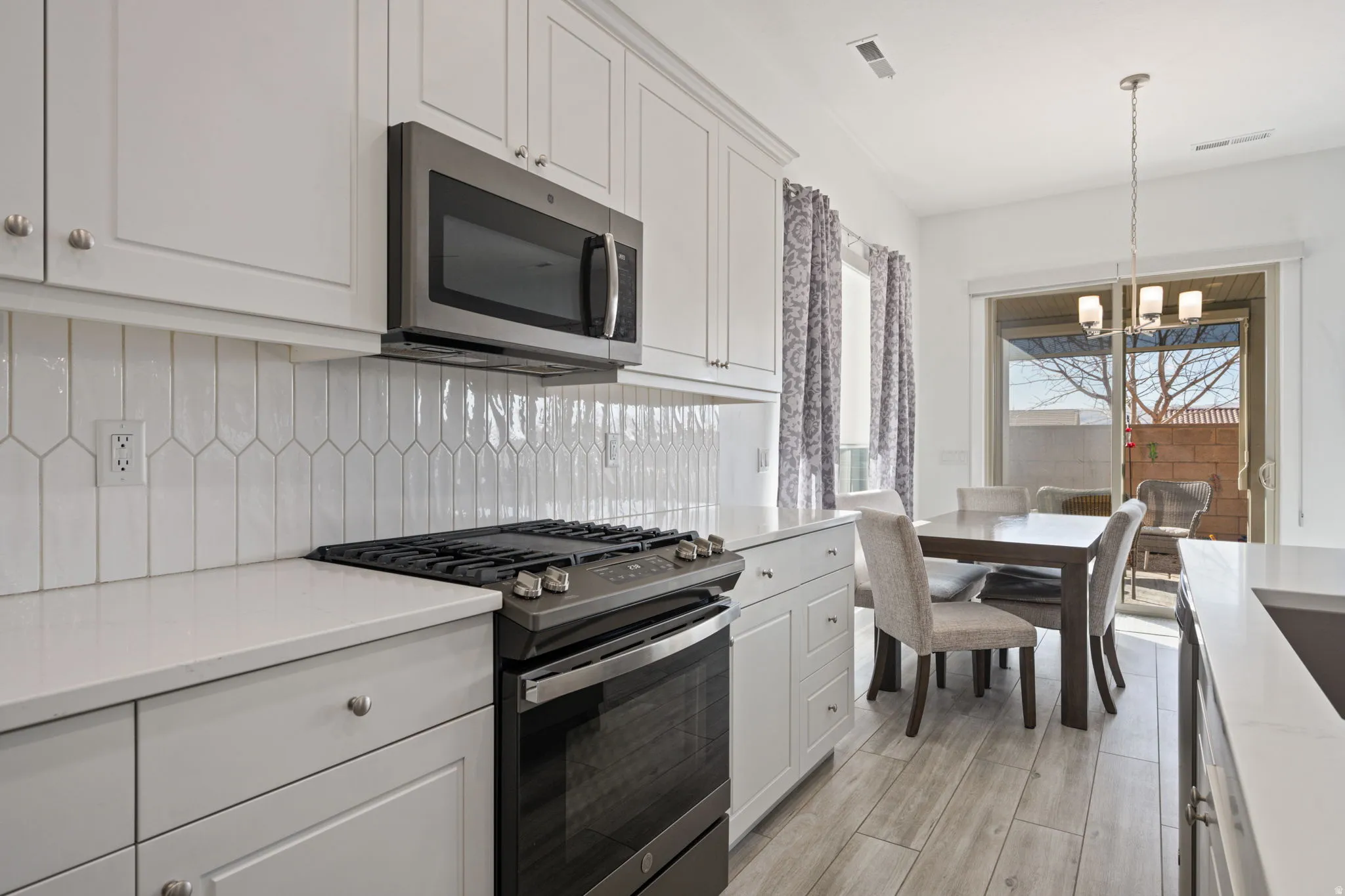 Kitchen with appliances with stainless steel finishes, white cabinetry, light stone counters, a chandelier, and decorative light fixtures