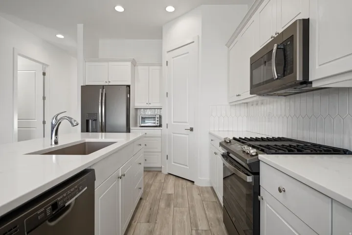 Kitchen featuring stainless steel appliances, recessed lighting, white cabinetry, light stone countertops, and light wood finished floors