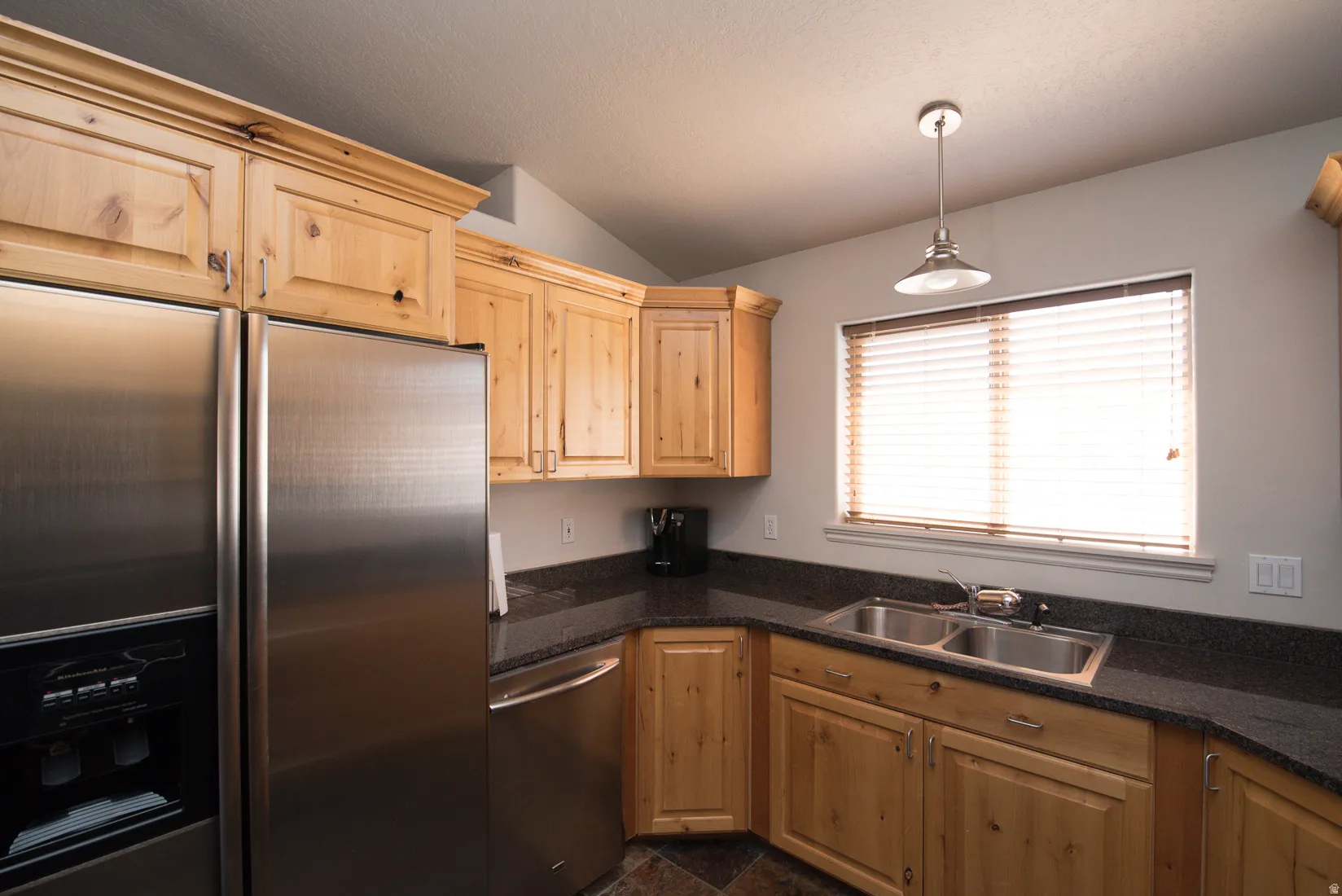 Kitchen featuring stainless steel appliances, decorative light fixtures, lofted ceiling, and light brown cabinets