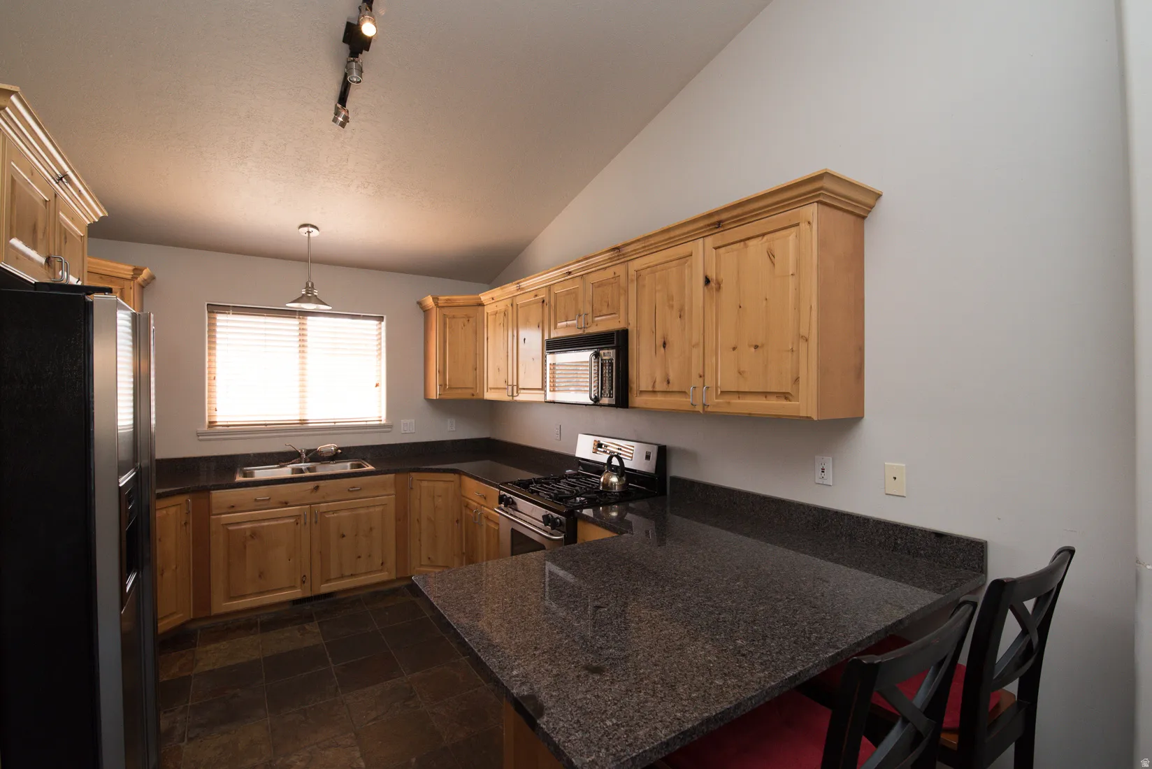 Kitchen featuring stainless steel appliances, a peninsula, vaulted ceiling, track lighting, and decorative light fixtures