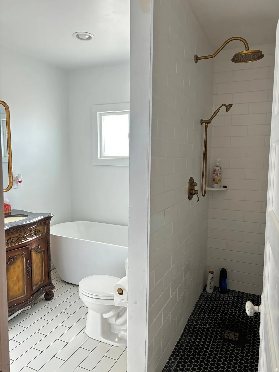 Full bath featuring vanity, a freestanding tub, tiled shower, and light tile patterned flooring
