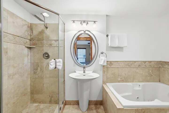 Bathroom featuring a glass-enclosed shower, a built-in tub, and a pedestal sink