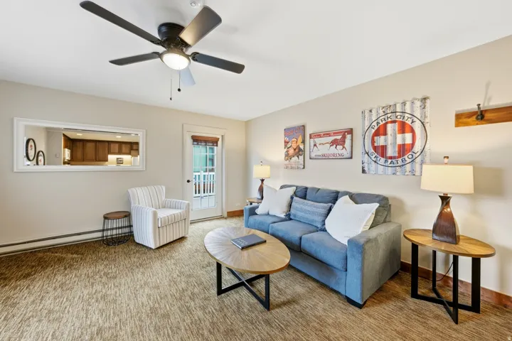 Living area featuring a ceiling fan with integrated lighting, a full-lite exterior door, and a wall-mounted mirror reflecting kitchen cabinetry