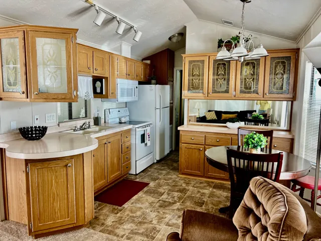 Kitchen featuring glass fronted cabinets, suspended lighting, white appliances, wood finish cabinetry, and light countertops