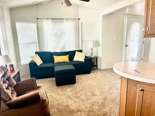 Living area with healthy amount of natural light, light colored carpet, vaulted ceiling, and a ceiling fan