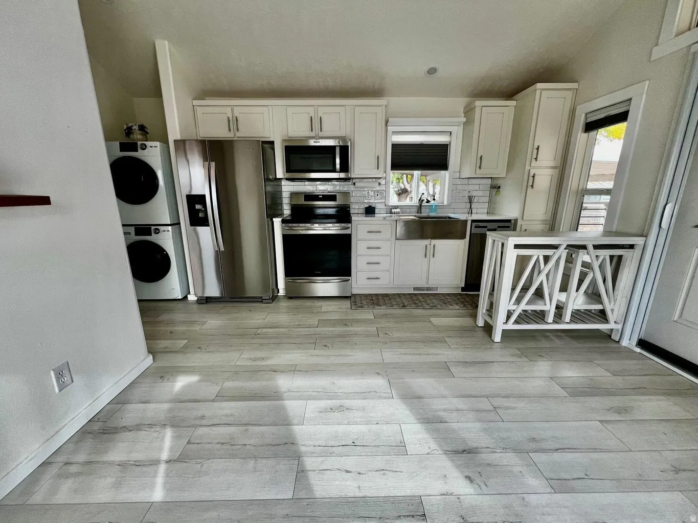 Kitchen with appliances with stainless steel finishes, backsplash, white cabinets, light wood-style floors, and estacked washer and dryer