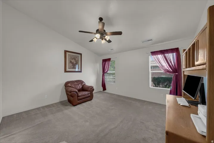 Unfurnished room featuring vaulted ceiling, light colored carpet, a ceiling fan, and a desk