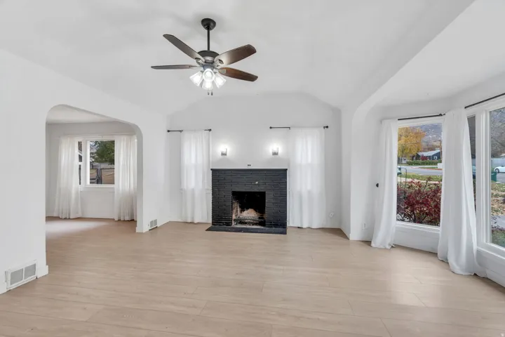 Unfurnished living room featuring vaulted ceiling, light wood finished floors, arched walkways, a brick fireplace, and a ceiling fan