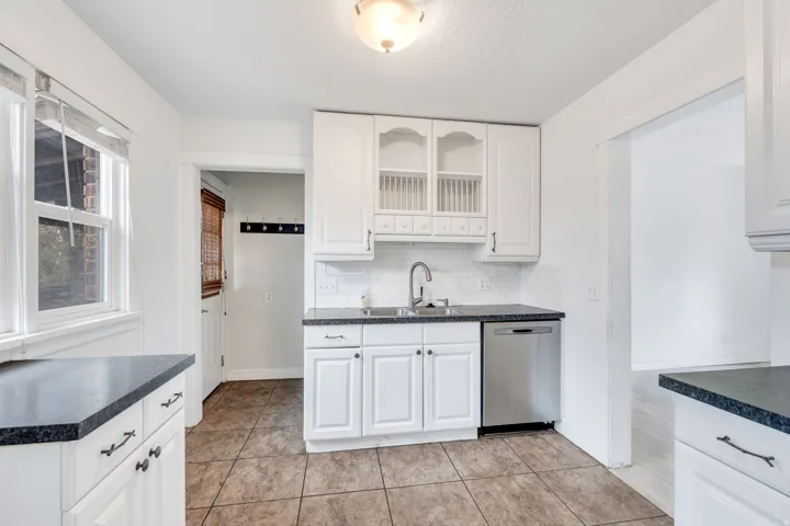 Kitchen with dark countertops, white cabinetry, backsplash, and stainless steel dishwasher