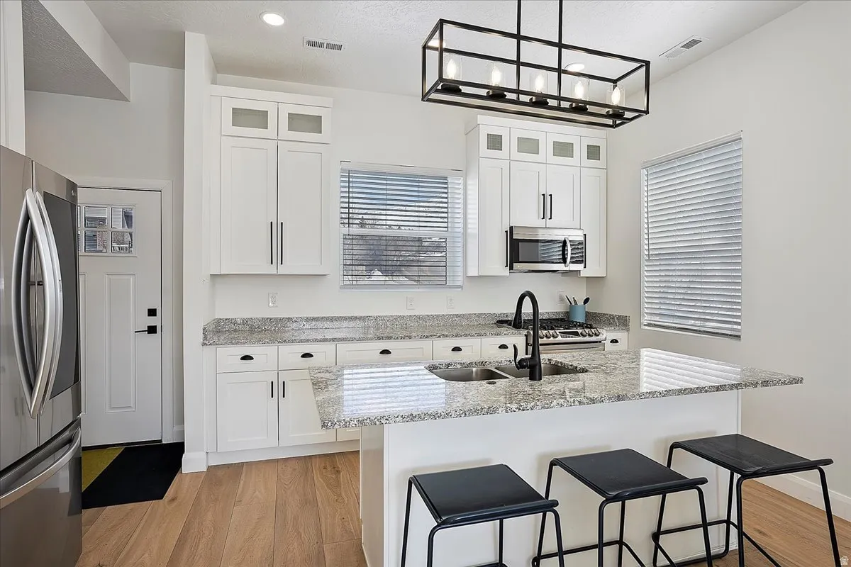 Kitchen with light stone countertops, a breakfast bar area, stainless steel appliances, glass insert cabinets, and light wood-style floors