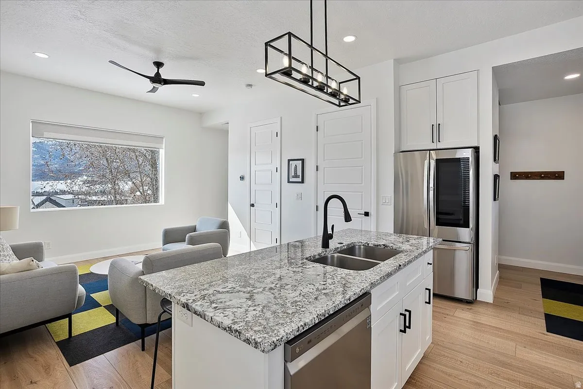 Kitchen featuring open floor plan, stainless steel appliances, light wood finished floors, light stone counters, and white cabinets