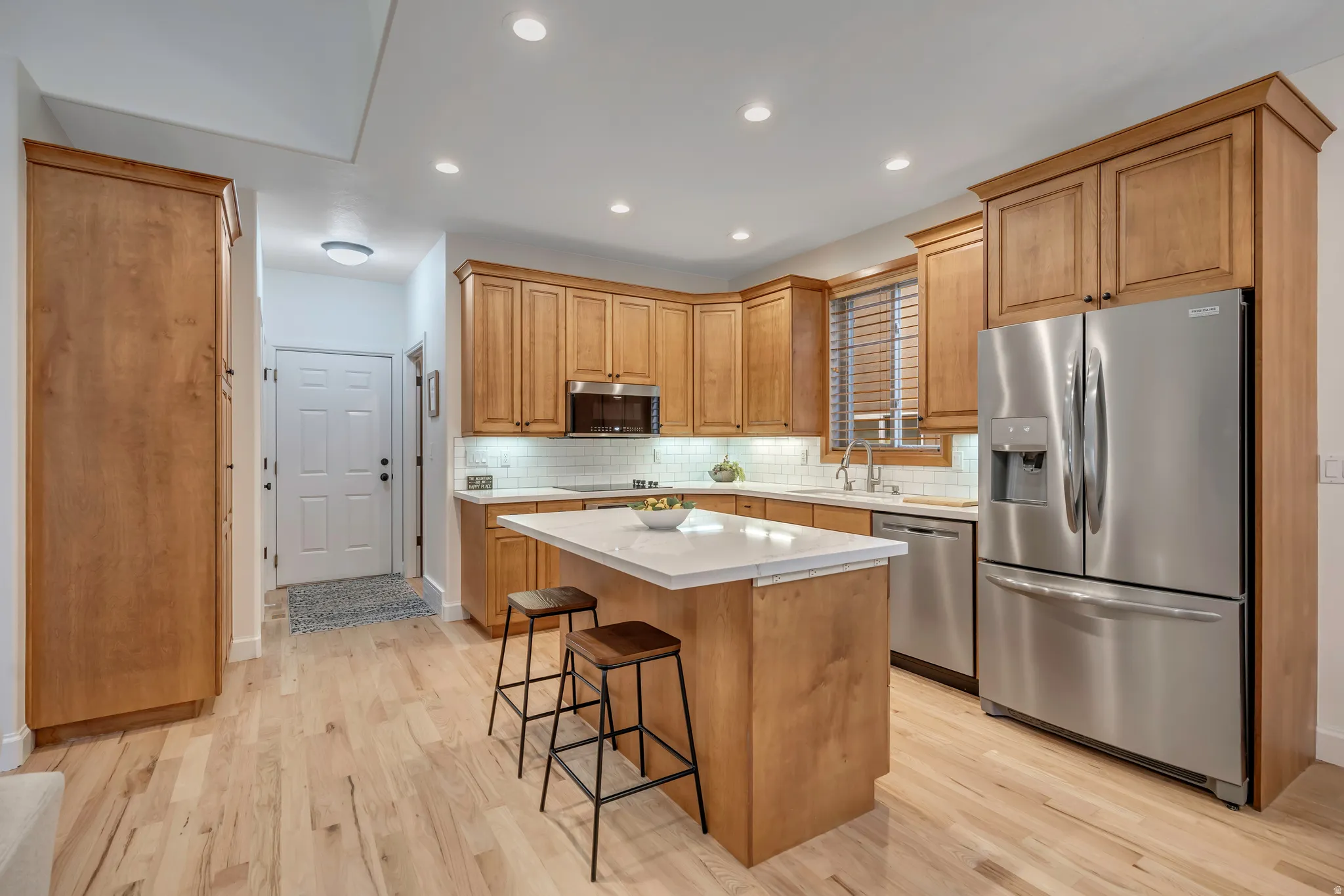 Kitchen featuring appliances with stainless steel finishes, tasteful backsplash, a kitchen island, light wood-style flooring, and a kitchen breakfast bar