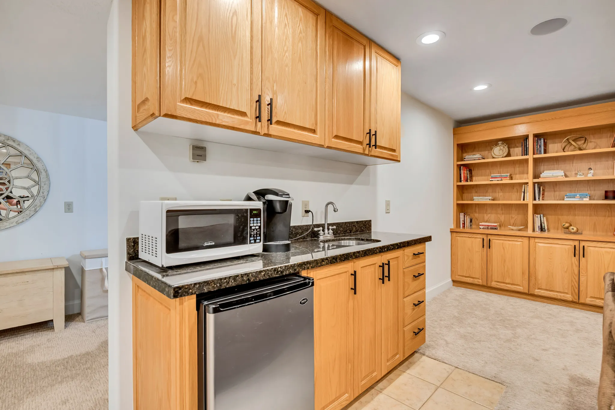 Basement family room featuring wet bar that includes  microwave, light brown cabinetry, and dark stone counters
