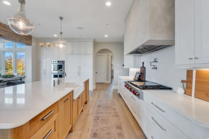 Kitchen with arched walkways, light wood-type flooring, recessed lighting, white cabinetry, and light stone counters