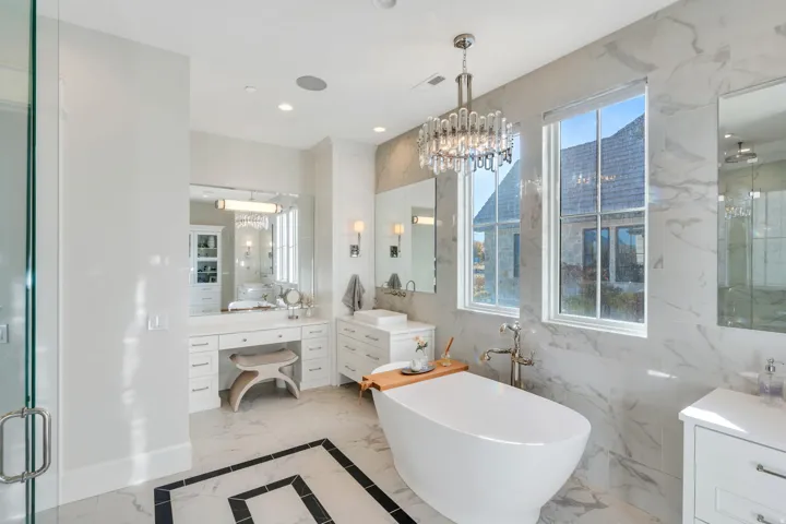 Full bathroom featuring light marble finish flooring, vanity, a marble finish shower, a soaking tub, and a chandelier