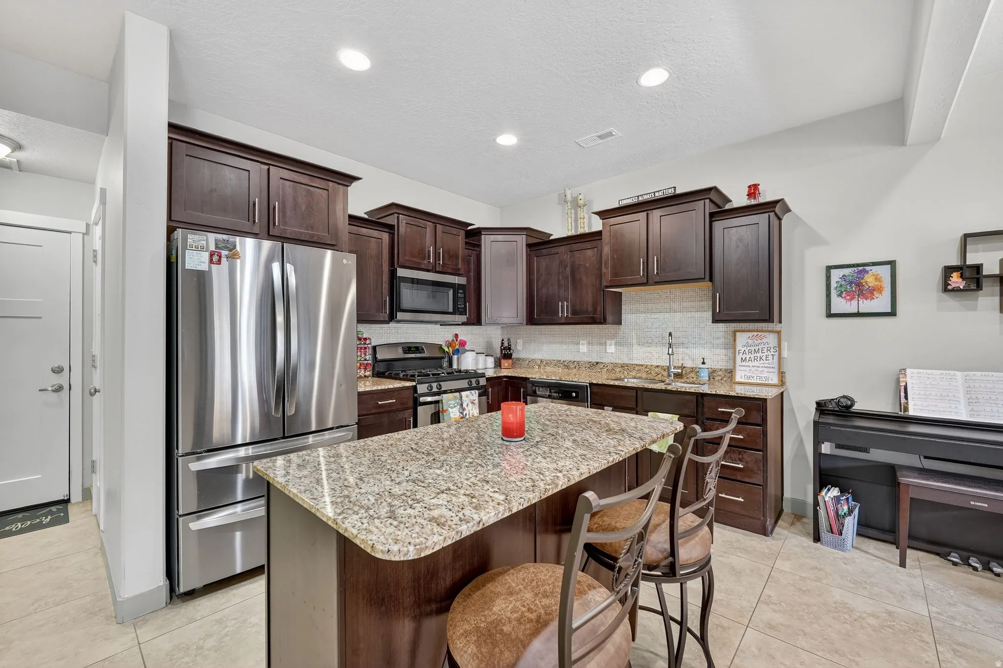 Kitchen featuring dark brown cabinetry, appliances with stainless steel finishes, light tile patterned floors, a breakfast bar, and light stone countertops