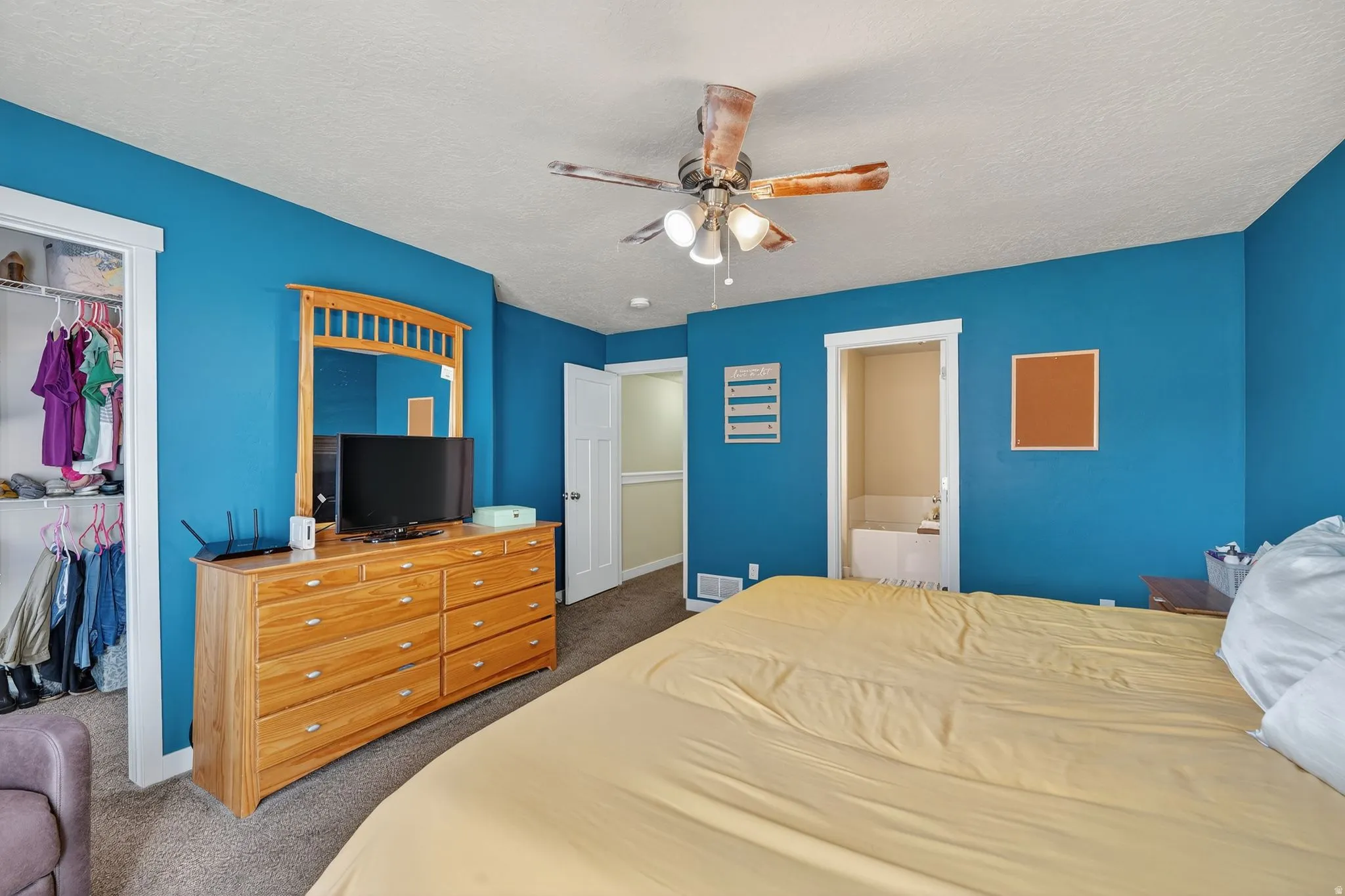 Bedroom with dark carpet, a ceiling fan, a textured ceiling, a closet, and ensuite bath
