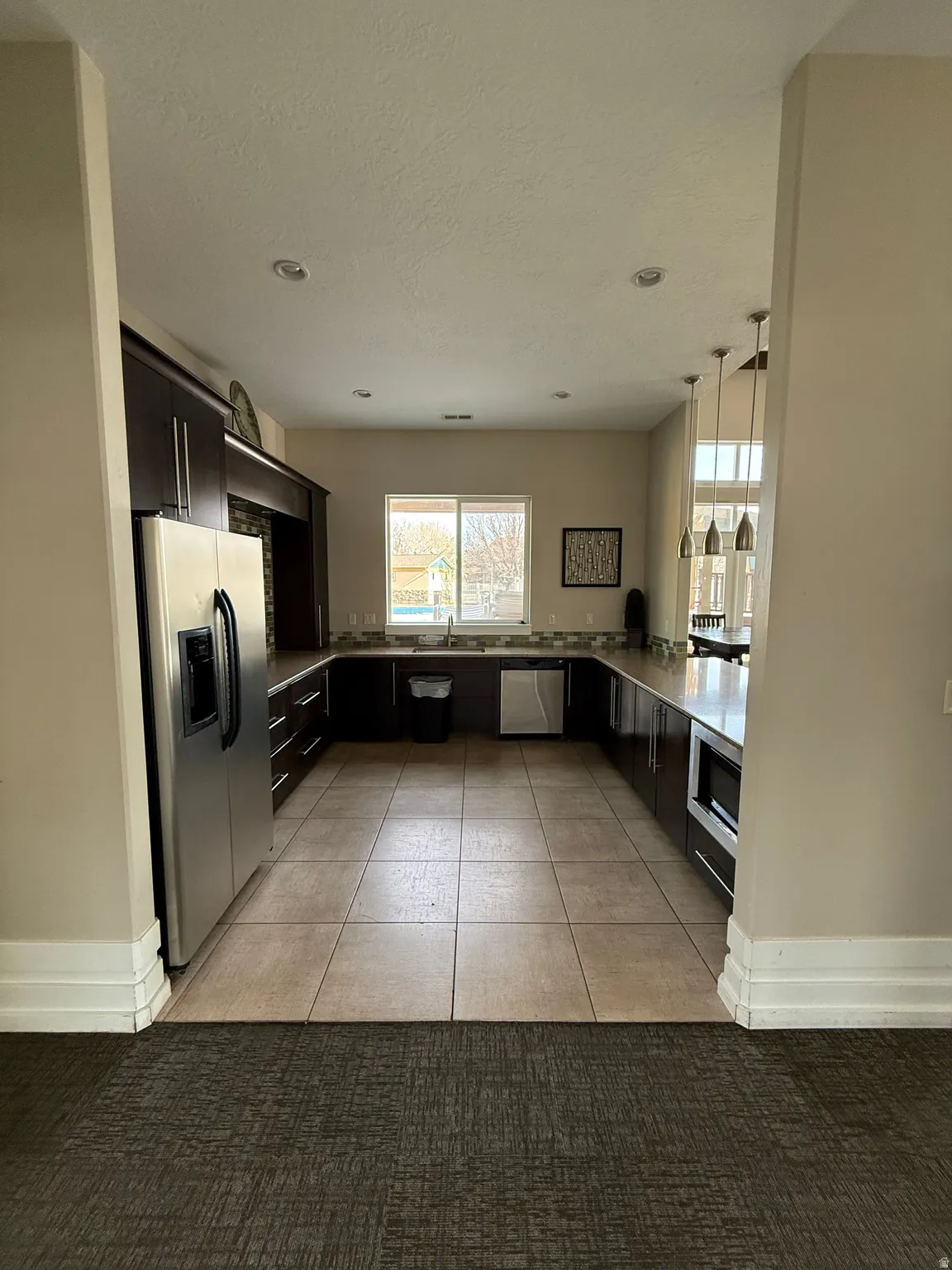 Kitchen featuring stainless steel appliances, light tile patterned flooring, light countertops, hanging light fixtures, and a textured ceiling