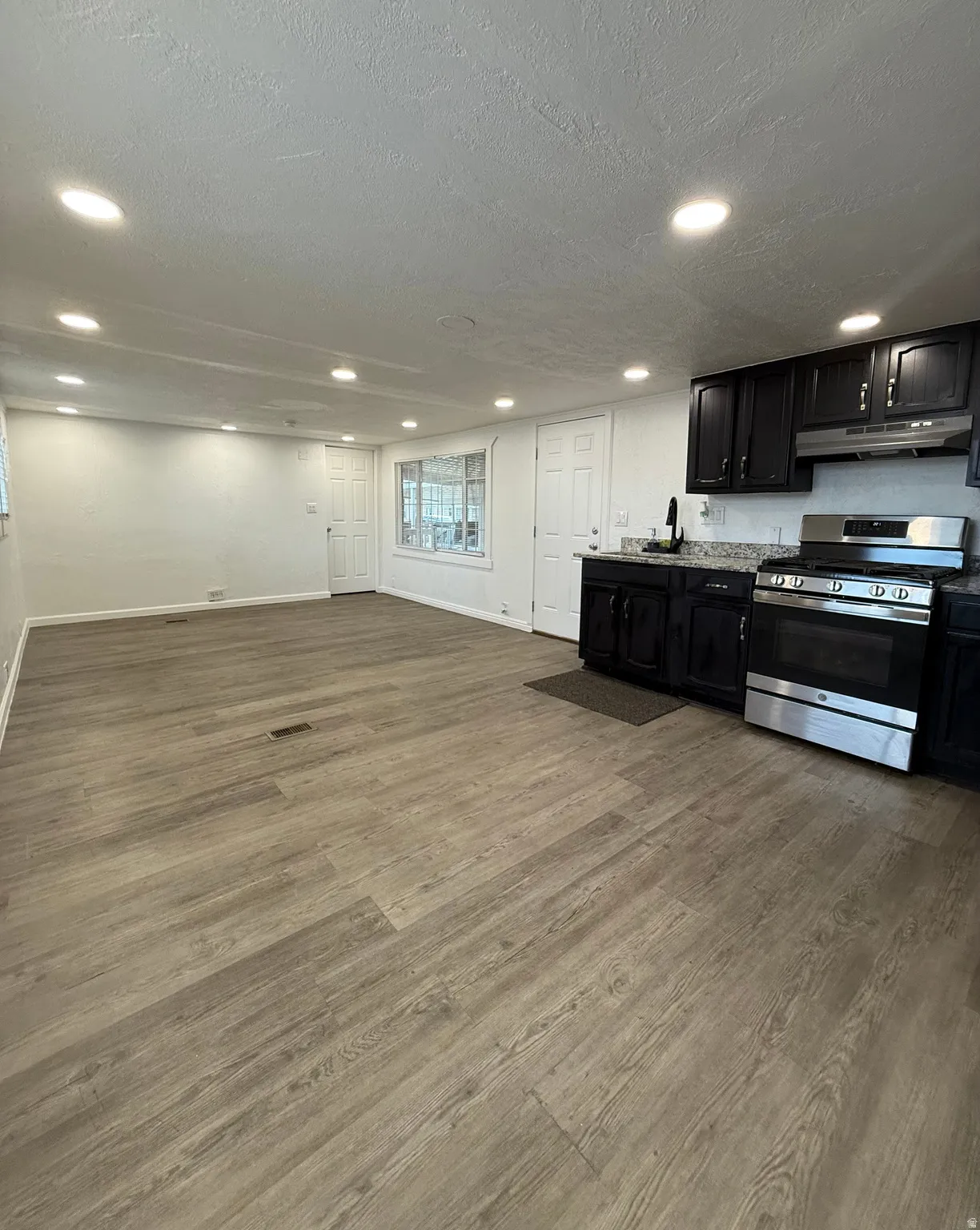 Kitchen featuring stainless steel gas range, dark cabinets, light wood finished floors, a textured ceiling, and recessed lighting