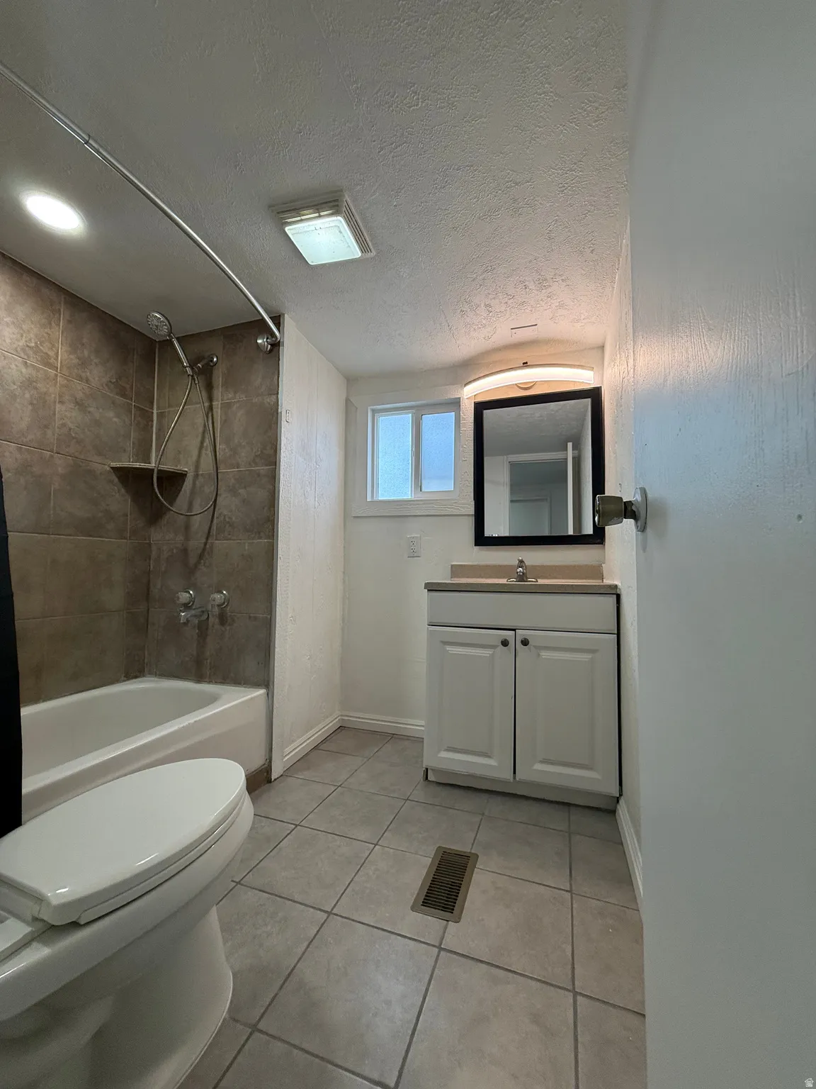 Full bath with light tile patterned floors, vanity, bathing tub / shower combination, and a textured ceiling