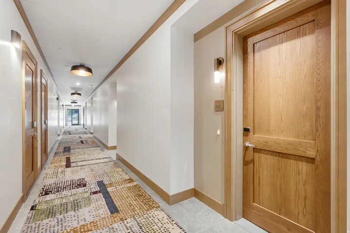 Corridor featuring wood-finish doors, wall-mounted sconces, ceiling-mounted lighting, and a patterned runner