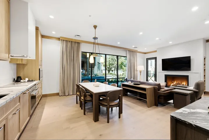Open concept living area featuring light wood-finish flooring, a contemporary fireplace, and a kitchen with light wood cabinetry and stone countertops