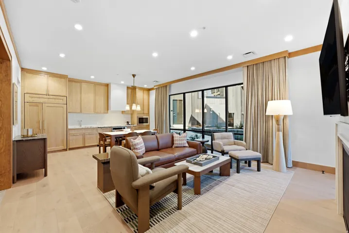 Open-concept living area featuring light wood-finish flooring, recessed lighting, expansive windows, and a kitchen with integrated paneled appliances and a tile backsplash