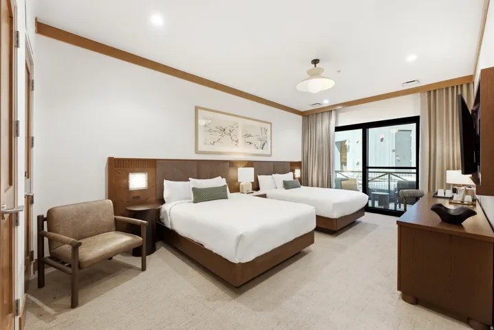 Spacious room featuring two beds, a private balcony with exterior railing, wood-finish flooring, and a built-in wood-finish headboard with integrated lighting