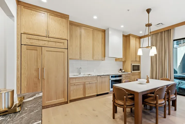 Wood-finish cabinetry, integrated refrigerator, white subway tile backsplash, light-toned wood-finish flooring, and recessed lighting