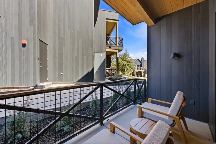 Private balcony with a slatted wood ceiling, dark wall-mounted exterior light fixture, and metal grid railing